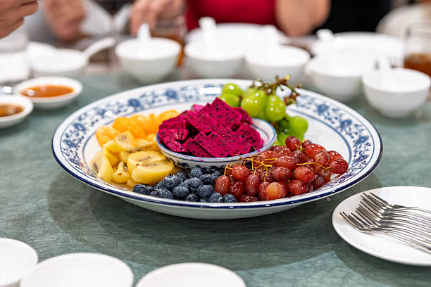 Close-up of assorted sliced fruits including dragon fruit, kiwi, mandarin orange, grapes, and blueberries arranged on a plate at a restaurant table.
