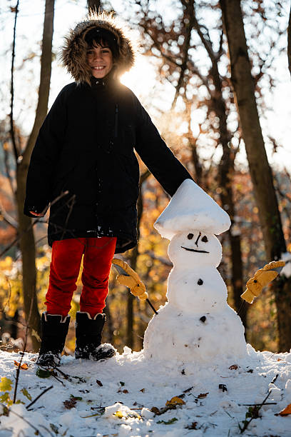istock Boy enjoying winter with snowman in forest 2240698302