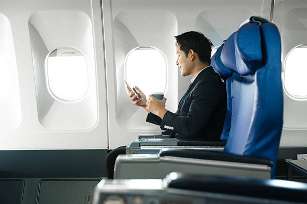 istock Young Asian executive excels in first class, multitasking with digital tablet, laptop and smartphone. Travel in style, work with grace. 2240699281
