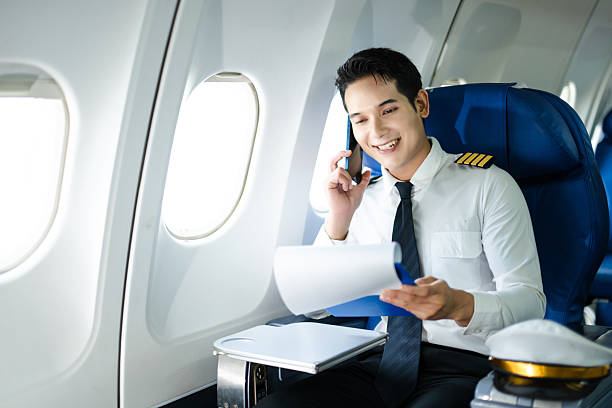 istock Asian Confident male pilot in uniform leaning at the passenger seat while standing inside of the airplane flight cockpit during takeoff and checking flight plan 2240699340