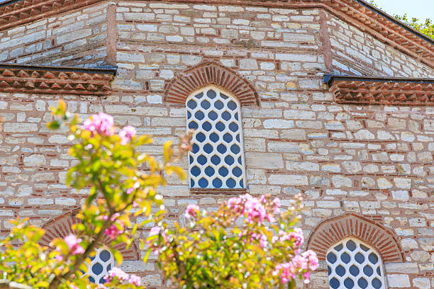 Historic brick and stone building with arched windows and blooming flowers.