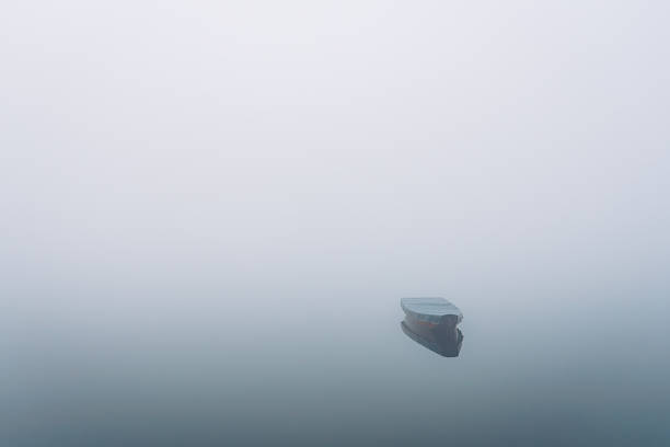 A solitary boat floating on still water in dense fog, symbolizing loneliness, sadness, and the passage of time.