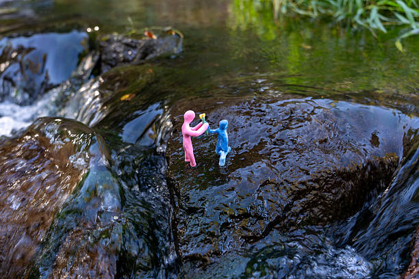 Small plasticine figurines on river rocks with flower exchange, artistic clay sculpture in natural environment