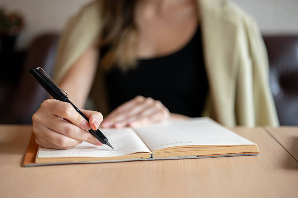 istock Close up woman's hand holding fountain pen writing in notebook on table while sits on sofa in a cafe 2240704061