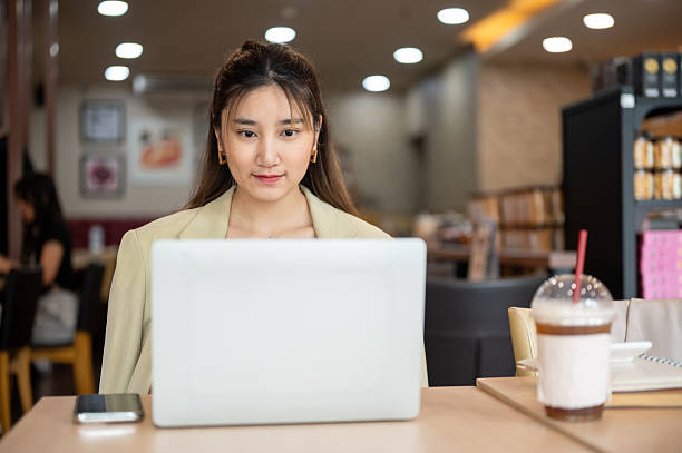 istock Asian woman looking and using the laptop doing assignment or watching video in a cafe or coffee shop 2240704275