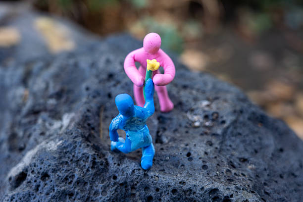 Pink and blue plasticine characters interacting – one offering a flower on a rock with blurred nature background
