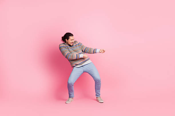 A vibrant man exudes liveliness and joy against a vivid pink backdrop, dressed in a fashionable printed sweater and jeans, capturing a casual and youthful lifestyle moment.