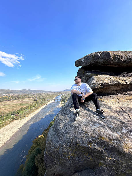 istock Man Sitting on Cliff Overlooking River and Valley 2240707906