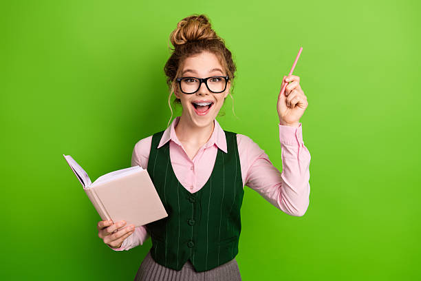 istock Happy young female student in a stylish uniform holding a book and pen while making a thoughtful gesture 2240712873