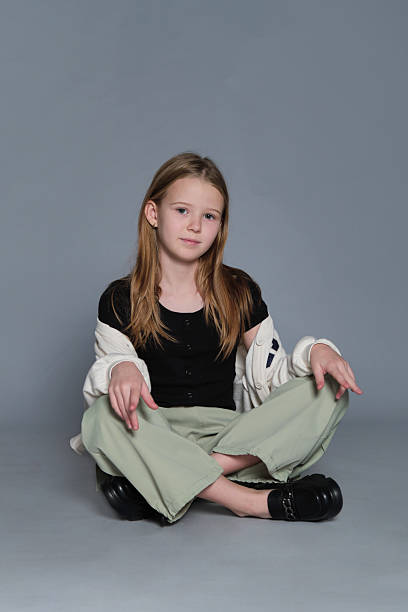 A young girl sits cross-legged on the floor with a calm expression. This simple studio portrait highlights themes of childhood identity and growing confidence in modern society.