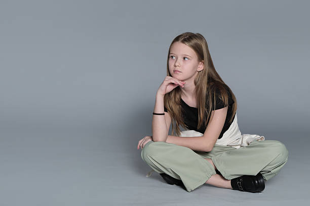 istock A child is seated on the floor in a neutral studio setting, looking directly at the camera. The shot connects with ideas of adolescence, self-awareness, and the search for individuality. 2240713591