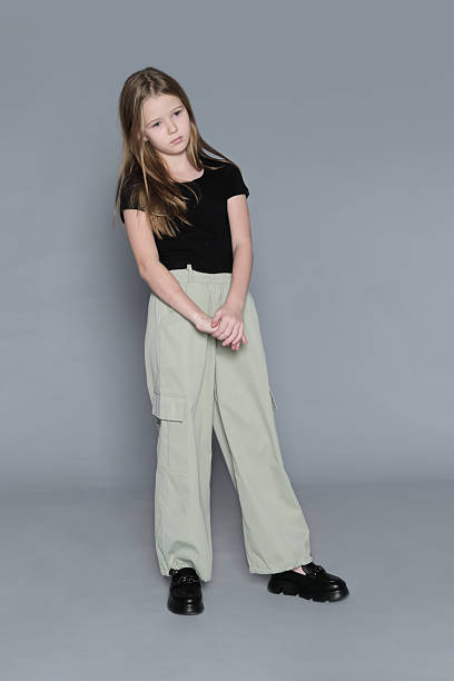 istock A young girl stands with her hands clasped, gazing thoughtfully in a neutral studio. This quiet and reflective moment speaks to the emotional depth often overlooked in childhood. 2240714044