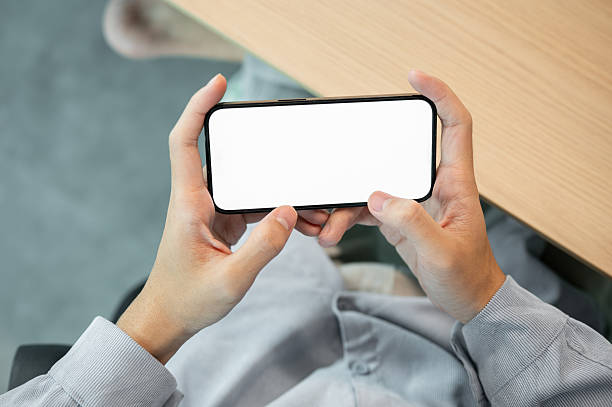 istock Blank screen smartphone holding horizontally with both hand while sitting at wooden table in a cafe. 2240717057