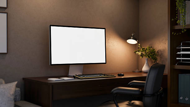 istock Blank screen computer under lamp light on wooden table with leather swivel chair in a dim lit room. 2240717914