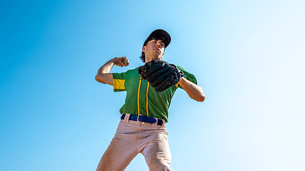 istock Baseball Player in Mid-pitch, Green and Yellow Uniform, Clear Blue Sky 2240718187