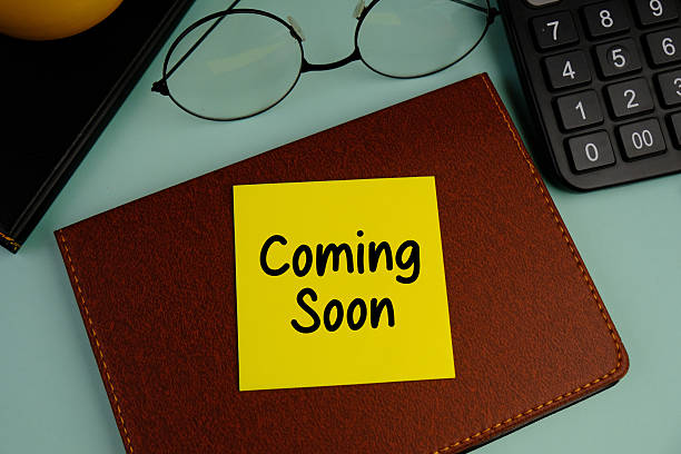Adhesive Note with Text Coming Soon surrounding by colorful office tools, green background.