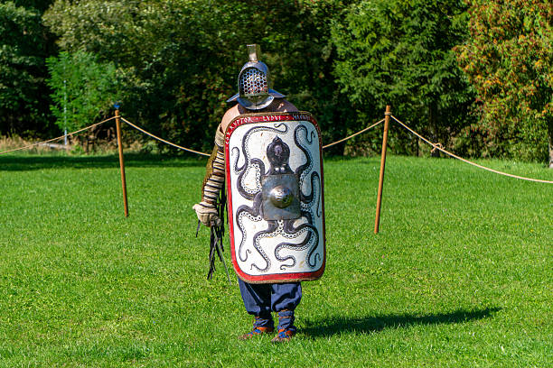 Częstochowa, Silesian Voivodeship, Poland - september 20, 2025 Roman reenactor dressed as gladiator stands on grassy field holding large shield decorated with octopus motif during historical performance at Juromania festival in Poland.
