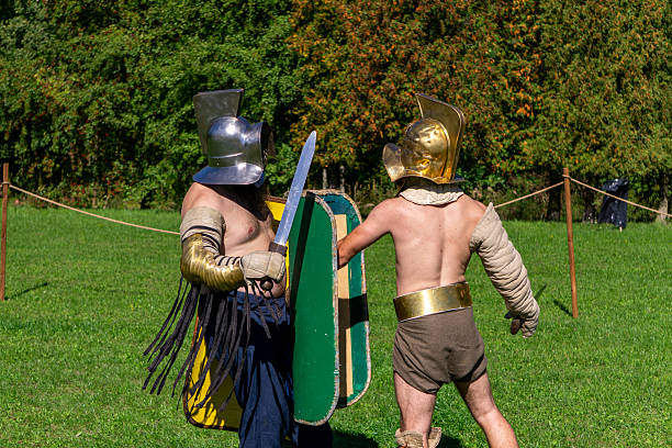 Częstochowa, Silesian Voivodeship, Poland - september 20, 2025 Roman reenactors wearing golden and silver helmets engage in sword combat on grassy field, performing a gladiator duel at the Juromania historical festival in Poland.