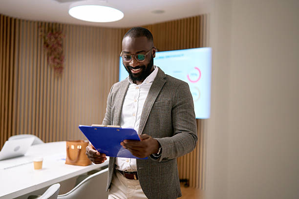 istock Black businessman smiling holding clipboard in modern office 2240725087