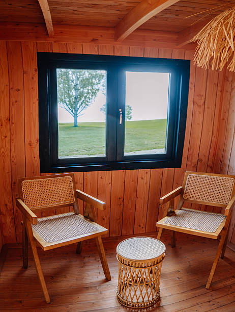 istock Cozy wooden interior with two rattan armchairs and a small wicker table by a window offering a scenic outdoor view. Warm, minimalist and inviting space. 2240729990