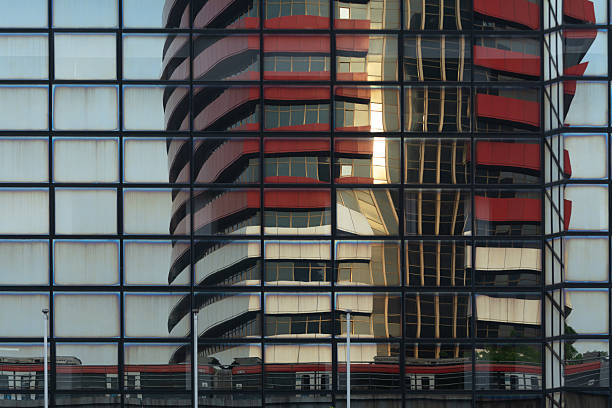Stock image of a modern skyscraper exterior showcasing reflective glass windows illuminated by the warm sunlight in the afternoon. The architecture highlights geometric lines and mirror-like surfaces, creating a bright urban atmosphere. Perfect for illustrating concepts of business, finance, real estate, architecture, and modern city development.