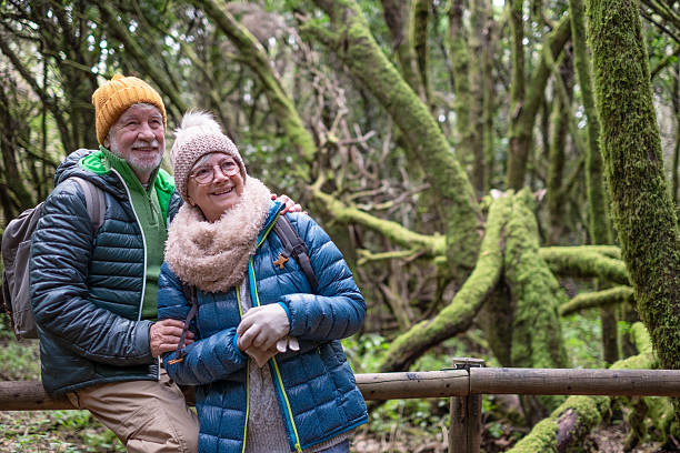 istock Active senior couple embracing enjoying winter excursion in a mountain forest with moss covered trunks. Joyful elderly couple traveling together in Garajonay national park of La Gomera 2240734288