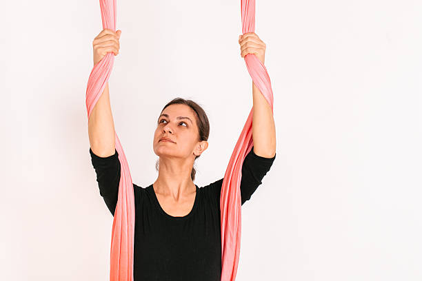 A young female aerial yoga instructor holding pink aerial silks, demonstrating the starting grip position. Indoor studio, fitness tutorial concept. Part of a step-by-step aerial silk instruction series. AERIAL_SILK_TUTORIAL_02_of_100