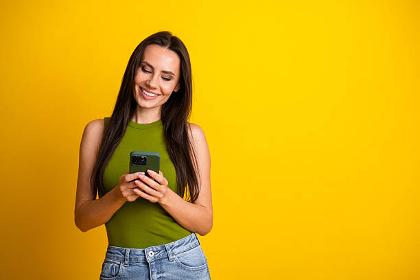 istock Attractive young woman smiling and using a smartphone against a bright yellow background for lifestyle advertising 2240737261