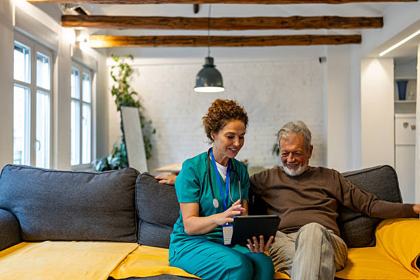 istock Caring Nurse And Elderly Man Share Tablet Conversation In Cozy Home Living Room 2240740109