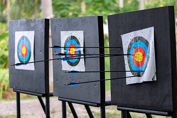 Three archery targets lined up outdoors, showing the results of intense practice with multiple arrows deeply embedded in the target faces, highlighting successful shots and training.