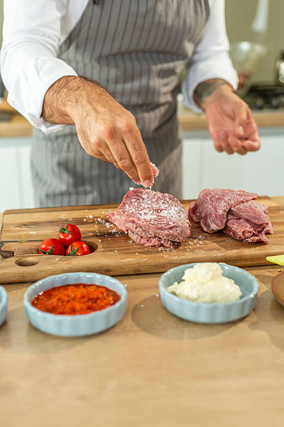 istock Chef sprinkling salt on fresh red meat in a modern kitchen 2240744291