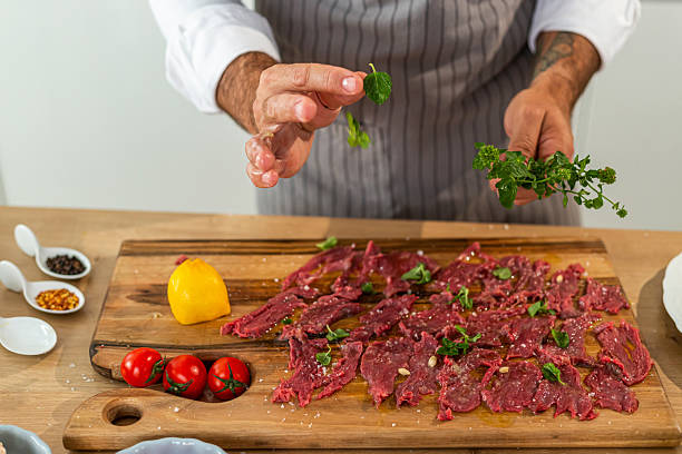 istock Chef adding fresh herbs to carpaccio on wooden cutting board 2240744293