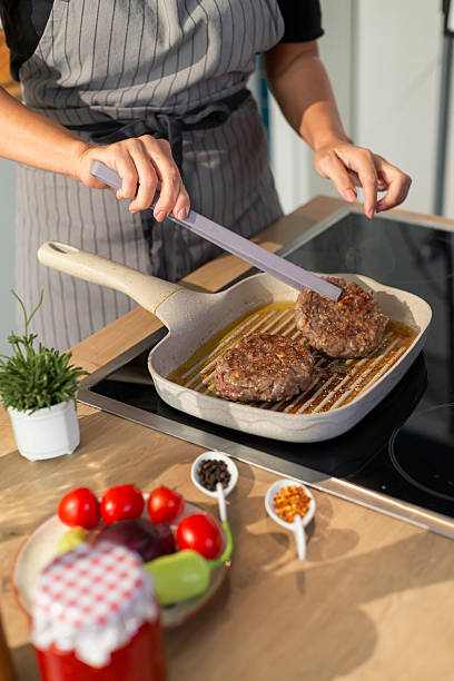 istock Woman cooking hamburgers in modern kitchen using grill pan 2240744298