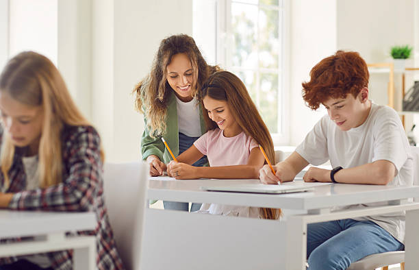 istock Teacher Helping Schoolgirl With Classwork In Classroom 2240753088
