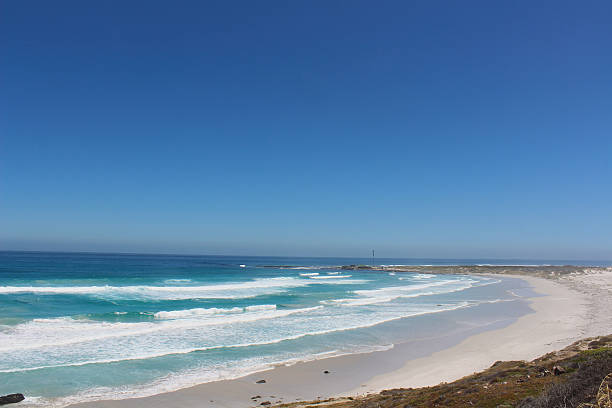 A peaceful beach scene with waves gently rolling onto smooth sand. A distant headland adds depth to the composition, while the clear sky and soft lighting evoke calm and relaxation. Ideal for travel, lifestyle, or nature-focused content.