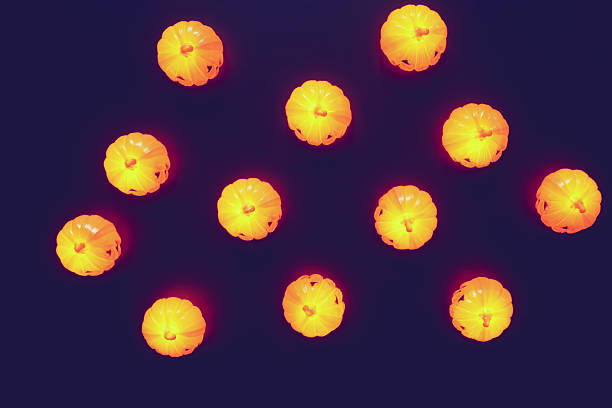 Minimal Halloween-themed composition featuring glowing orange pumpkin lights arranged neatly on a dark background. The simple layout and vivid color contrast evoke a sense of playful warmth and seasonal festivity. Copy space for text, directly above - Autumn background, Halloween