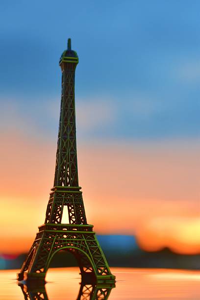 A miniature Eiffel Tower stands gracefully against a vibrant sunset sky, symbolizing dreams of travel and the charm of Parisian evenings. Chasing Paris dreams under golden skies.
