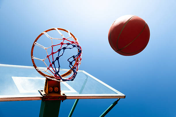 Basketball ball and hoop with net outdoors against blue sky