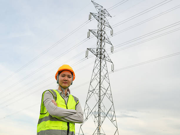 istock Young Female Electrical Engineer with Safety Gear Standing Confidently Near High Voltage Power Lines with Clear Blue Sky in the Background 2240776711