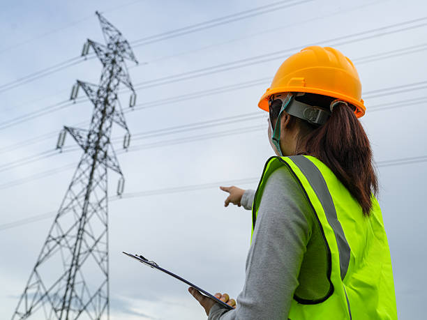 istock Construction worker in safety gear inspecting power lines against a cloudy sky while holding a clipboard for performance assessment and safety checks 2240776725