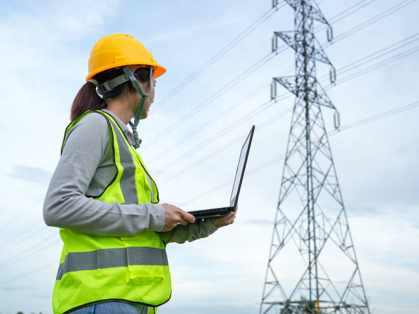 istock Worker with laptop in safety gear observing electrical power lines under cloudy sky at a utility site demonstrating modern technology in engineering 2240776779