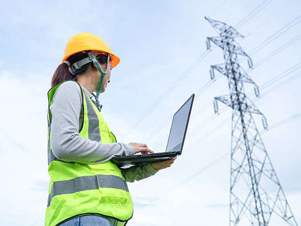istock Engineer in Safety Gear Using Laptop Outdoors Under High Voltage Power Lines for Energy Industry Infrastructure Project Management and Inspection 2240776794
