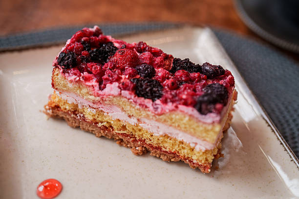 Close-up of a layered sponge cake topped with mixed berries and cream, served on a ceramic plate with berry sauce drops.