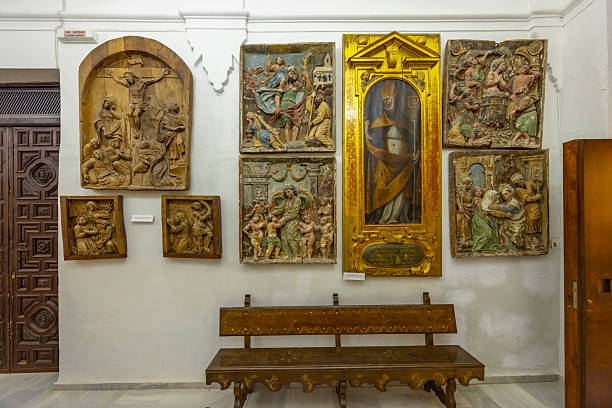 Gallery display featuring a collection of carved wooden reliefs and a framed saint painting in Baeza, Spain