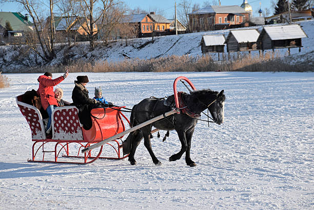 Suzdal, Russia - February 23, 2025: A family rides a horse-drawn sleigh on the frozen Kamenka River. Fun Russian traditions and activities in the city.