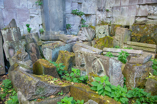 Weathered Roman stone relief with carved busts partially buried in tall grass along the Appian Way, showing erosion, age, and the integration of archaeological remains into the natural landscape.