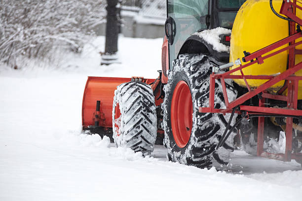 A tractor hauling a load of hay down a straight and snow-covered road.
