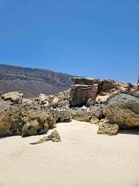 istock Rocky outcrops on white sandy beach under clear blue sky 2240799436