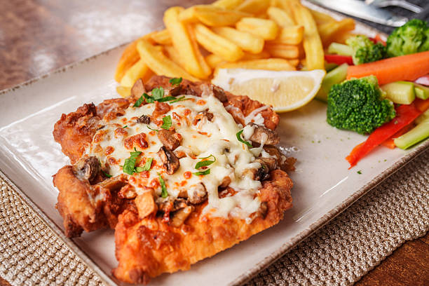 Crispy chicken schnitzel topped with creamy mushroom sauce and melted cheese, served alongside golden fries and steamed vegetables. A rich and comforting dish combining tender chicken, earthy flavors, and fresh seasonal sides.