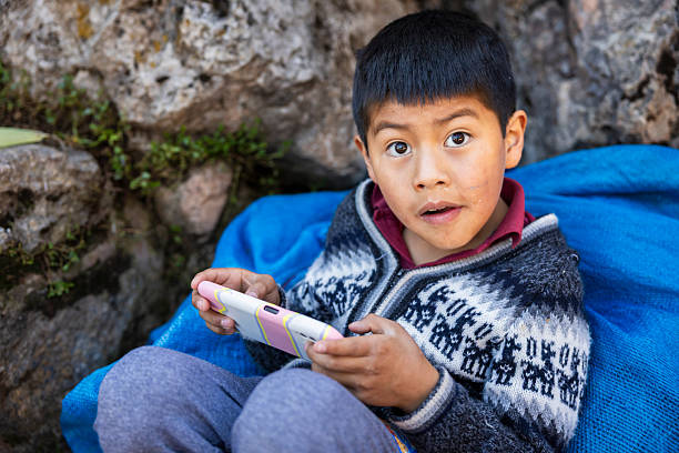 Peruvian young boy playing mobile game on smartphone, Sacred Valley, Peru. The Sacred Valley of the Incas or Urubamba Valley is a valley in the Andes  of Peru, close to the Inca capital of Cusco and below the ancient sacred city of Machu Picchu. The valley is generally understood to include everything between Pisac  and Ollantaytambo, parallel to the Urubamba River, or Vilcanota River or Wilcamayu, as this Sacred river is called when passing through the valley.